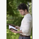 Man reading a book outdoors with greenery in the background